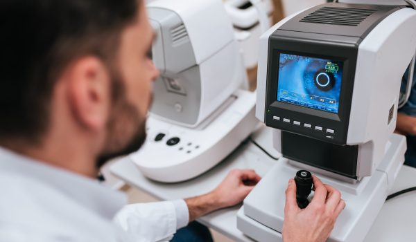 Handsome male doctor  ophthalmologist is checking the eye vision of attractive young woman in modern clinic. Doctor and patient in ophthalmology clinic.